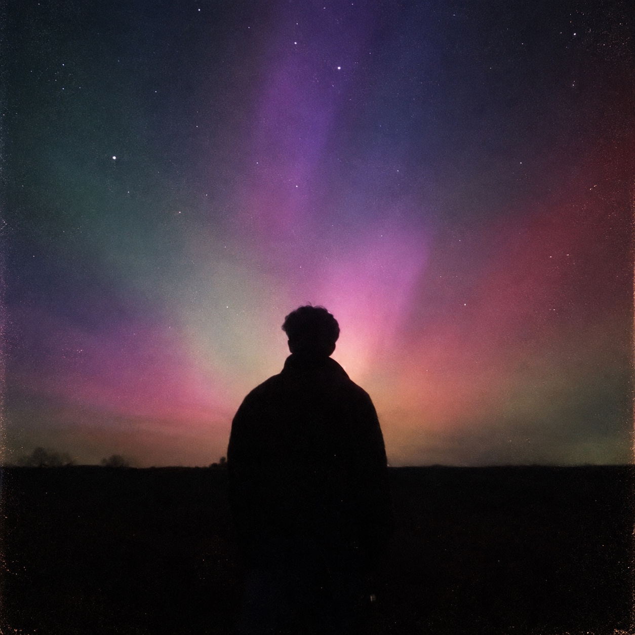 A silhouetted figure beneath a colourful aurora and starry night sky